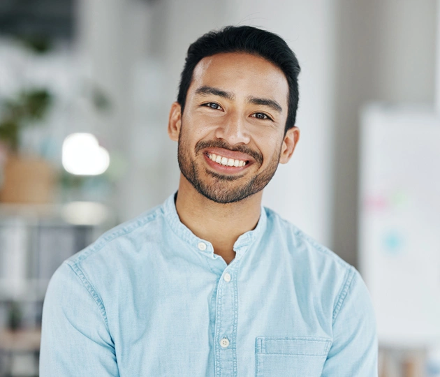 Smiling male dentist wearing light blue shirt in modern dental office setting.