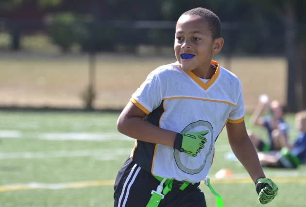 Young athlete in light blue shirt running on sunny sports field during practice.