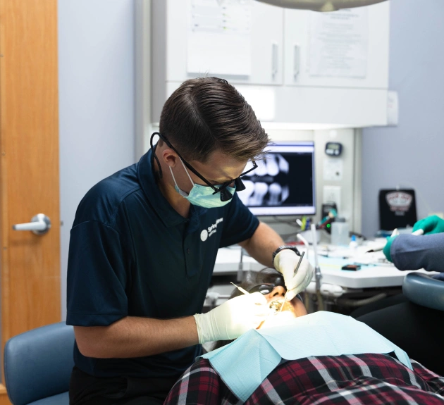 Dentist in protective gear examining patient in dental clinic operatory.