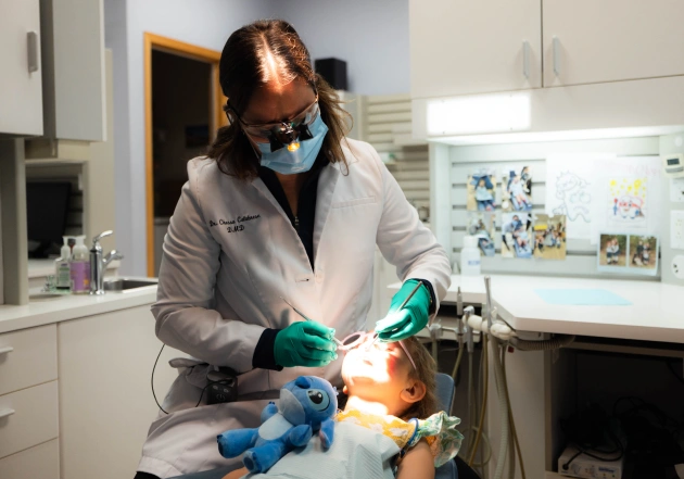 Dental hygienist in mask and gloves treating patient in modern dental office operatory.