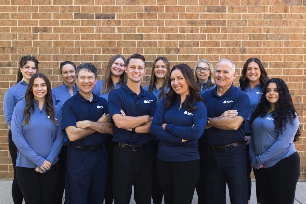 Spring View Dental team members posing together in blue uniforms against brick wall background.