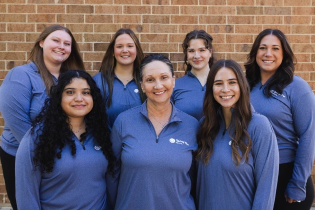 Spring View Dental team of seven women in blue uniforms standing together against brick wall.