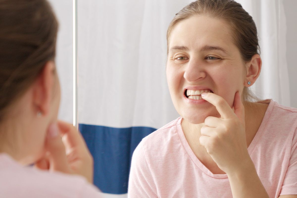 Adult woman examining wiggly tooth and gum health in mirror