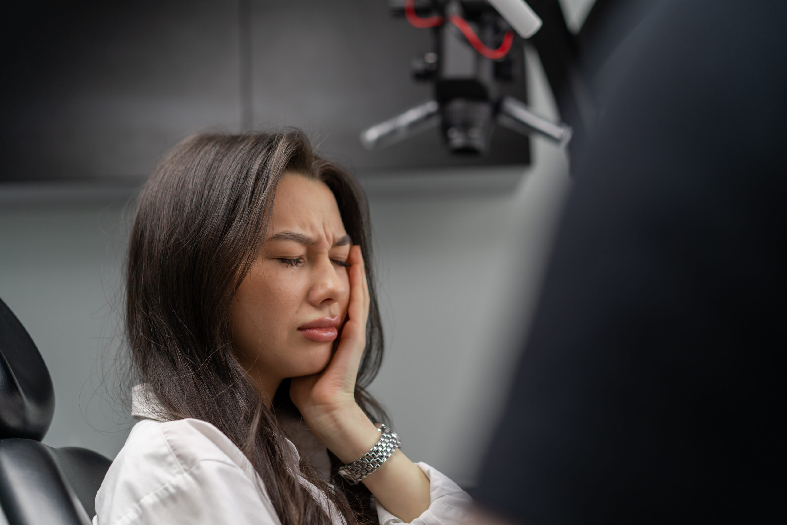 Woman experiencing severe tooth pain while delaying dental treatment at a dental clinic.
